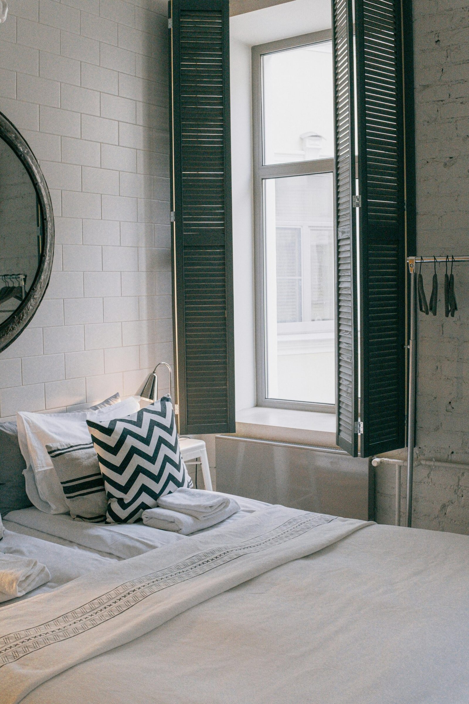 A cozy and stylish bedroom featuring modern decor and a sunlit window with shutter panels.